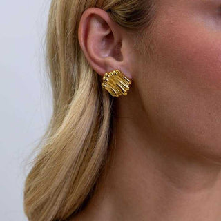 Gold earrings worn by a person with blonde hair against a white background