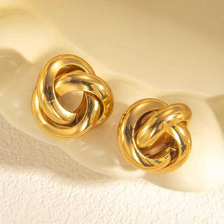 Pair of gold knot earrings on a textured beige surface