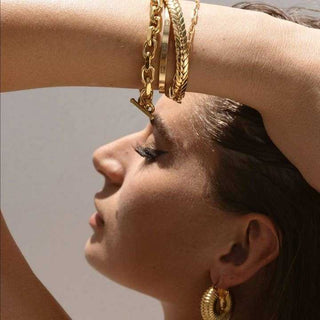 Woman wearing gold jewelry including bracelets and earrings against a neutral background