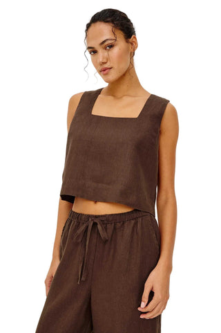 Woman wearing a brown sleeveless top and pants on a white background