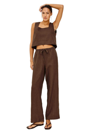 Woman wearing a brown sleeveless top and wide-leg pants on a white background