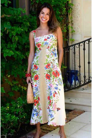 Woman wearing a floral dress standing outdoors with greenery and a building in the background.