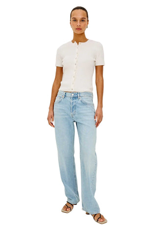 Woman wearing a white shirt and light blue jeans on a plain background