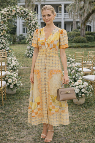Woman in a yellow checkered dress standing in a garden setting with floral decorations and chairs.