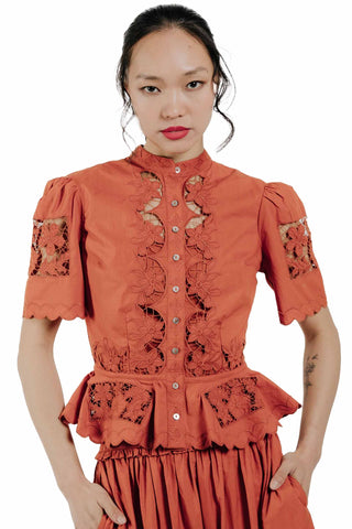 Love the Label Elizabeth Top in Cinnamon. Cinnamon orange top with intricate floral cutwork lace, high neck, puff sleeves, button front, and peplum hem 