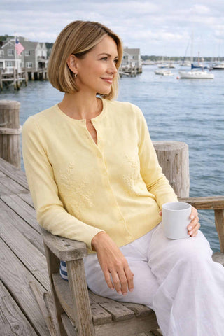 Woman in a yellow cardigan sitting by a waterfront holding a mug.