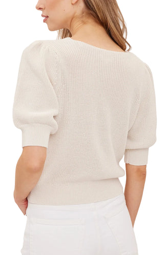 A woman shown from the back wearing a cream-colored knit sweater with short puff sleeves and white pants, against a plain light background.