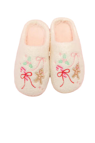 Cream-colored plush slippers with embroidered gingerbread men, red bows, and holly leaves, featuring pink fuzzy lining