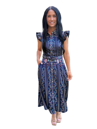 A woman wearing a navy blue patterned midi dress with cap sleeves and a tie waist, standing on a paved outdoor walkway.
