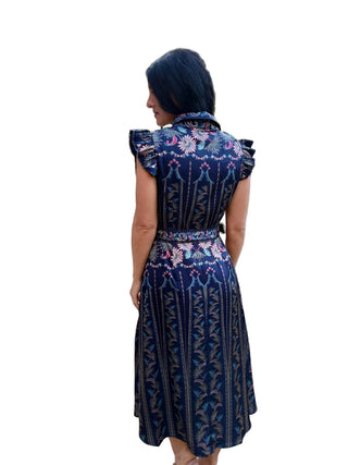 A woman wearing a navy blue patterned midi dress with floral and vertical stripe motifs, photographed from behind on an outdoor street sidewalk.