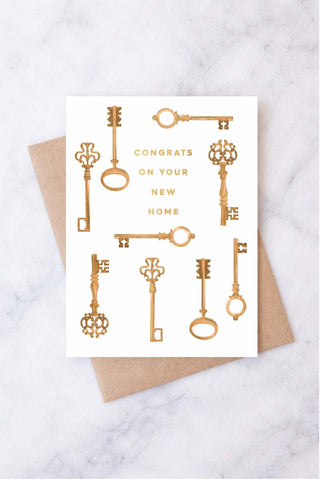 Greeting card with gold keys and 'Congrats on your new home' text on a white background, placed on a marble surface.