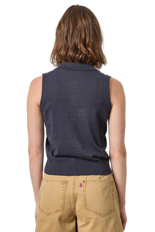 Person wearing a navy sleeveless sweater over a beige shirt on a plain background