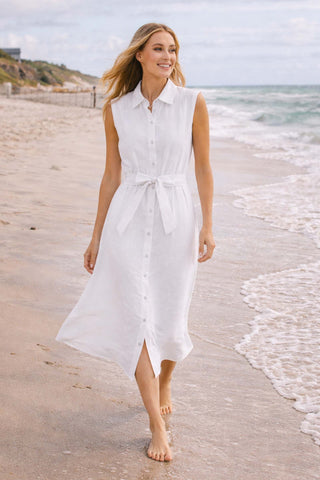 Woman in a white dress standing on a beach with ocean waves in the background