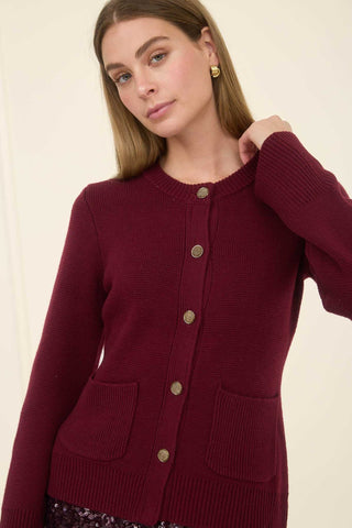 Woman wearing a burgundy cardigan with gold buttons on a beige background