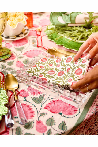 Table setting with floral tablecloth, cutlery, and a hand holding a folded napkin.