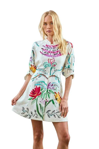 Woman wearing a floral dress with colorful designs on a blue background. Hunter Bell Molly Anniversary Print Dress