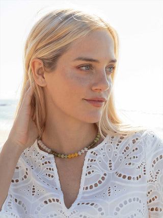 Woman wearing a white lace top and colorful beaded necklace against a bright background