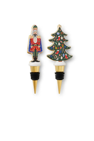 Two decorative wine stoppers featuring hand-painted nutcracker soldier and Christmas tree designs with gold metal stoppers and black rubber seals