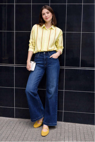 Woman wearing a yellow shirt and blue jeans against a black tiled wall.