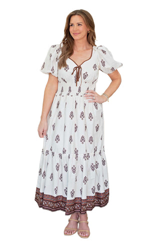 Moon River Puff Sleeve Pleated Midi Dress in Cream. cream midi dress with burgundy floral print, featuring puff sleeves, lace-up V-neckline with brown trim, and tiered pleated skirt with border print