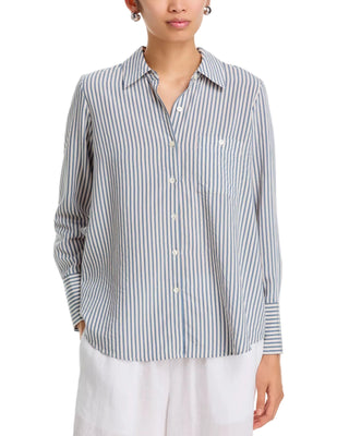 A woman wearing a long-sleeve button-front shirt with vertical blue and white stripes, paired with white pants, against a plain white background.