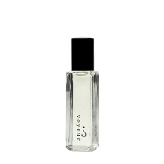 A clear glass perfume bottle with a black cap, featuring the brand name 'voyeur' printed vertically in black on the front, set against a plain white background.
