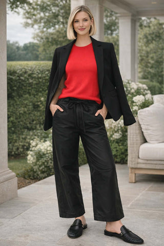 Woman in a red top and black pants standing on a patio with greenery in the background