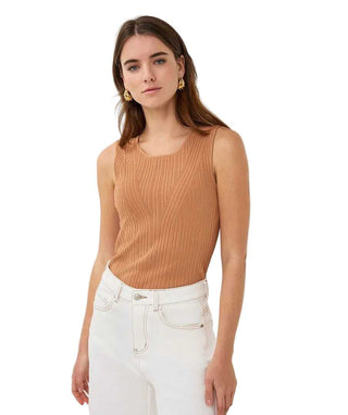 Woman wearing a brown ribbed tank top and white pants on a light gray background