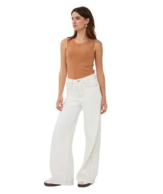 Woman wearing a brown ribbed tank top and white wide-leg pants on a white background