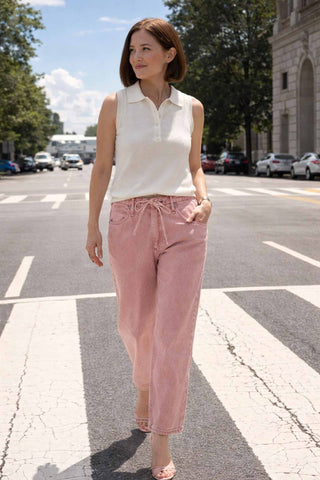 Woman walking on a street wearing a white sleeveless shirt and pink pants.