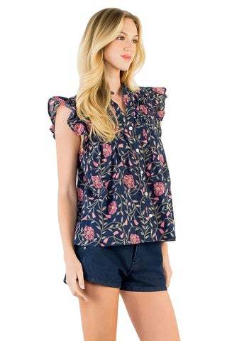 A woman modeling a navy blue sleeveless blouse with a pink and green floral print, paired with dark denim shorts, against a plain white studio background.