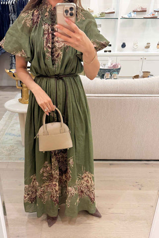 Woman taking a mirror selfie wearing a green floral dress in a store.