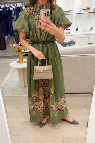 Woman taking a mirror selfie wearing a green floral dress in a store.