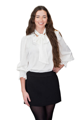 white long-sleeve blouse with oversized bow tie at neck and smocked cuffs