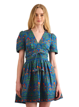 Hunter Bell Roan Dress in Midnight Garden. Floral mini dress in midnight garden print with deep V-neckline, puffed short sleeves, cinched waist with tie detail, and gathered skirt in blue, green, and orange hues