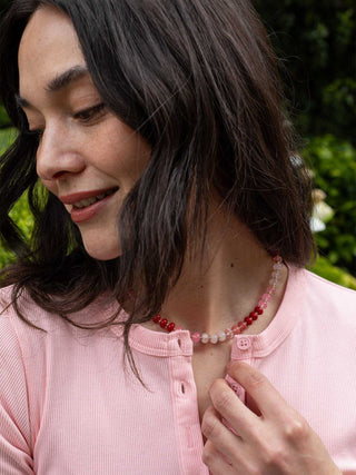 Woman wearing a pink shirt and red beaded necklace outdoors