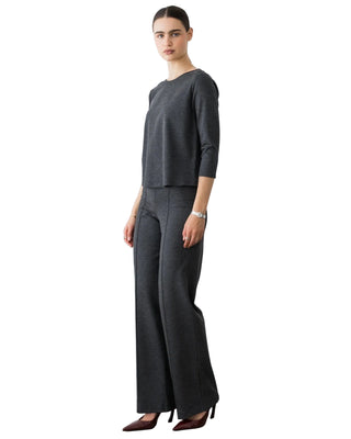 A woman modeling a dark gray two-piece knit set consisting of a three-quarter sleeve top and matching wide-leg trousers, paired with dark brown pointed-toe heels against a plain white studio background.