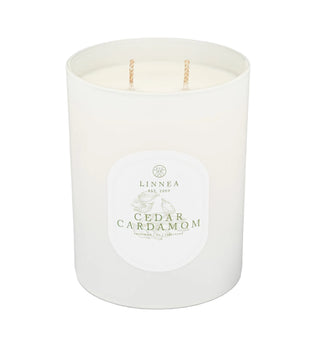 A white double-wick soy candle in a matte white glass jar with a circular white label reading LINNEA and CEDAR CARDAMOM, photographed on a clean white background.