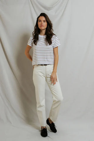 Woman wearing a striped shirt and white pants against a plain background