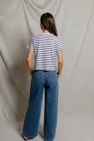 Person wearing a striped shirt and blue jeans standing against a plain background