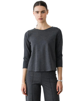 A woman modeling a dark gray three-quarter sleeve top and matching dark gray trousers against a plain light gray studio background.